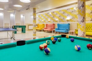 Sala gier w Domu Wczasowym Rudnik z bilardem, piłkarzykami i stołem do ping-ponga oraz kolorowymi fotelami.